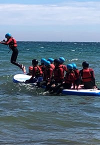 Our Charities – group of kids on sitting on top of a surfboard—- Our Charities - group of kids on sitting on top of a surfboard
